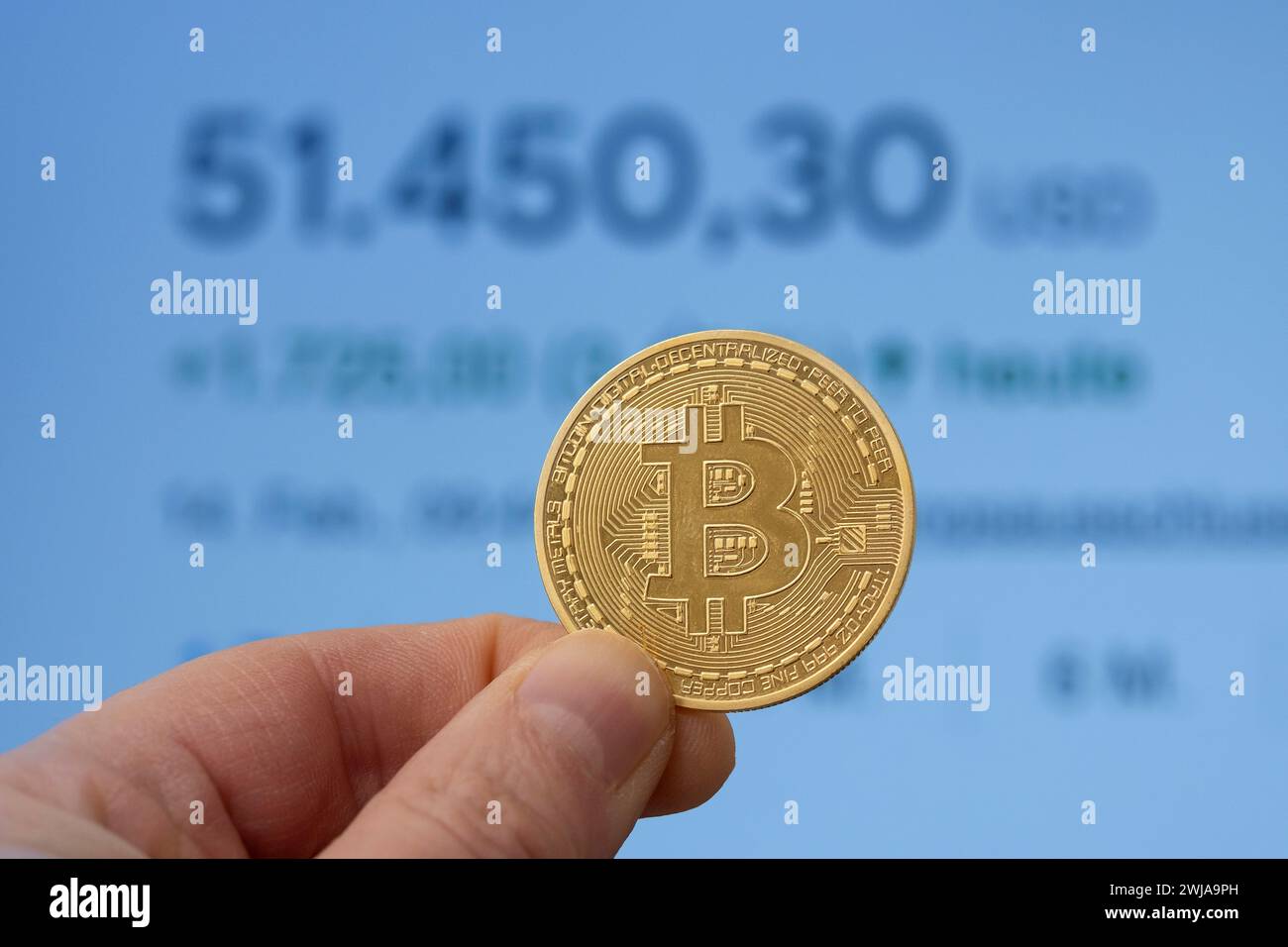 Bitcoin-Münze zwischen den Fingern vor einem Marktpreis von über 50.000 USD Stockfoto