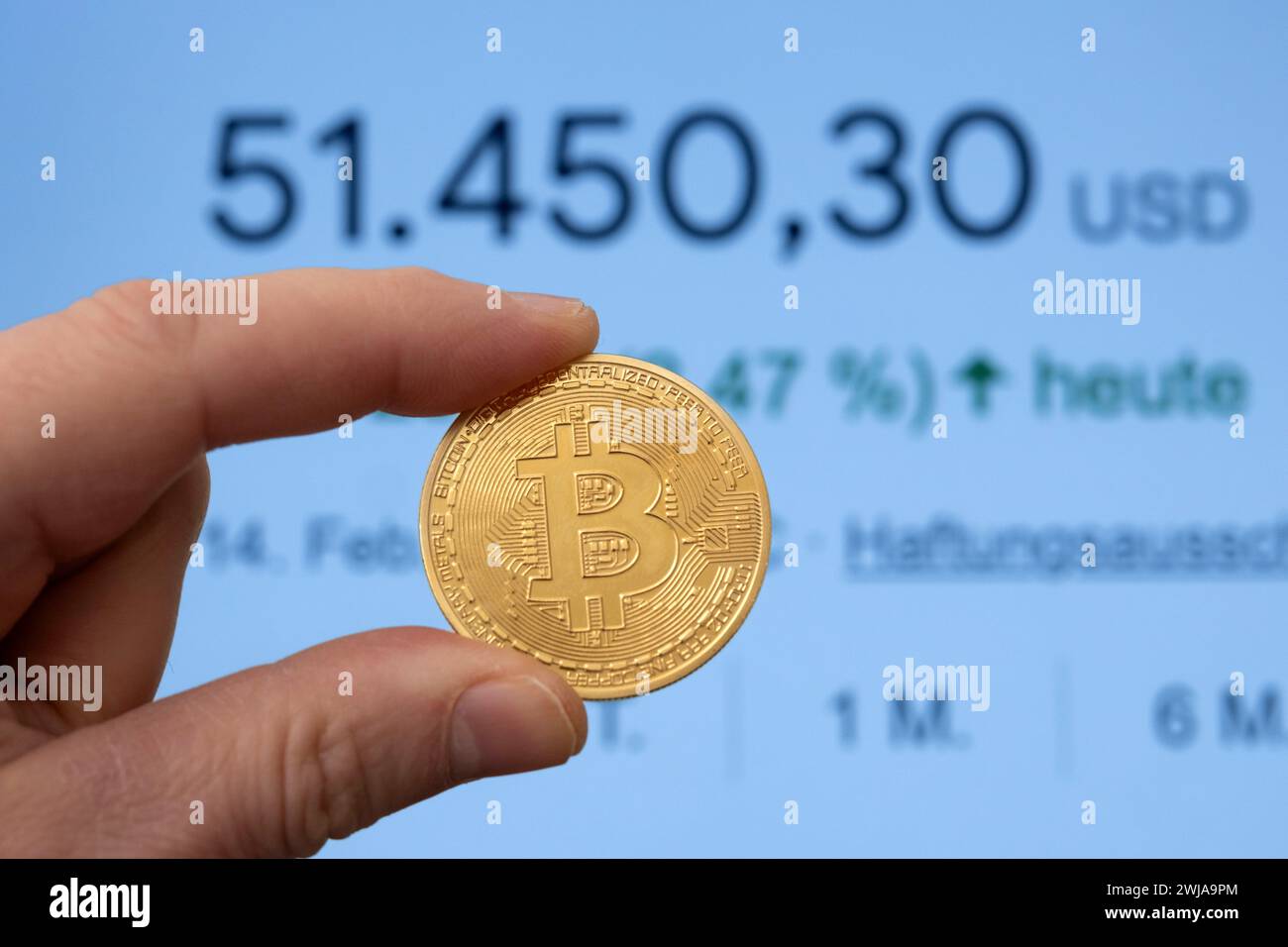 Bitcoin-Münze zwischen den Fingern vor einem Marktpreis von über 50.000 USD Stockfoto