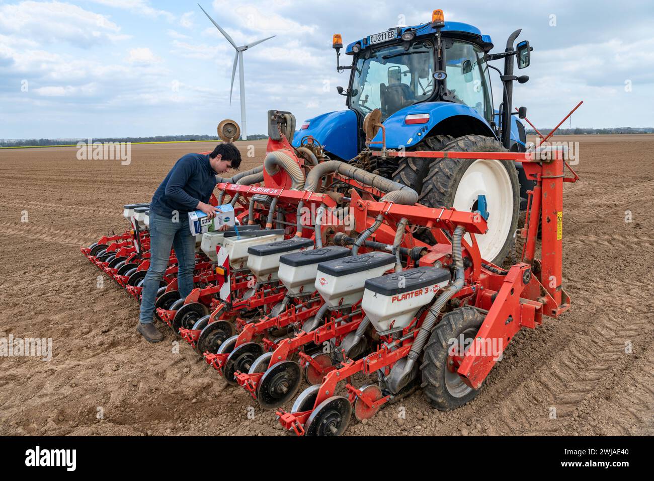 Aussaat von Zuckerrüben auf einem Feld im April mit einem Traktor und einer 12-reihigen Kuhn-Sämaschine. Landwirtschaftliche Angestellte, die Saatgutbehälter füllen, Zuckerrübensaat, in Sai Stockfoto