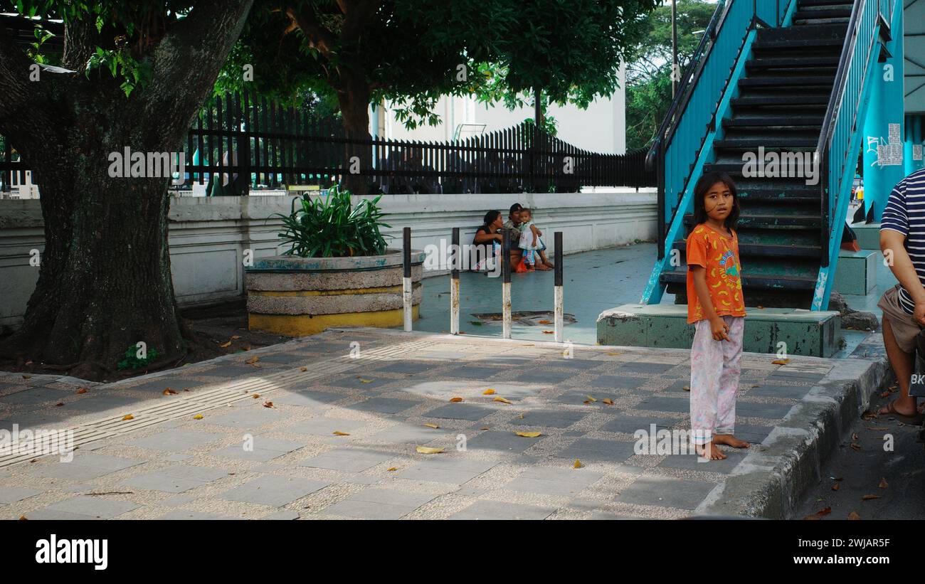 In Medan City steht ein obdachloses Mädchen allein vor dem Leben. Trotz aller Schwierigkeiten hält sie an Hoffnung fest, eine Erinnerung an Widerstandsfähigkeit im urbanen Chaos. Stockfoto