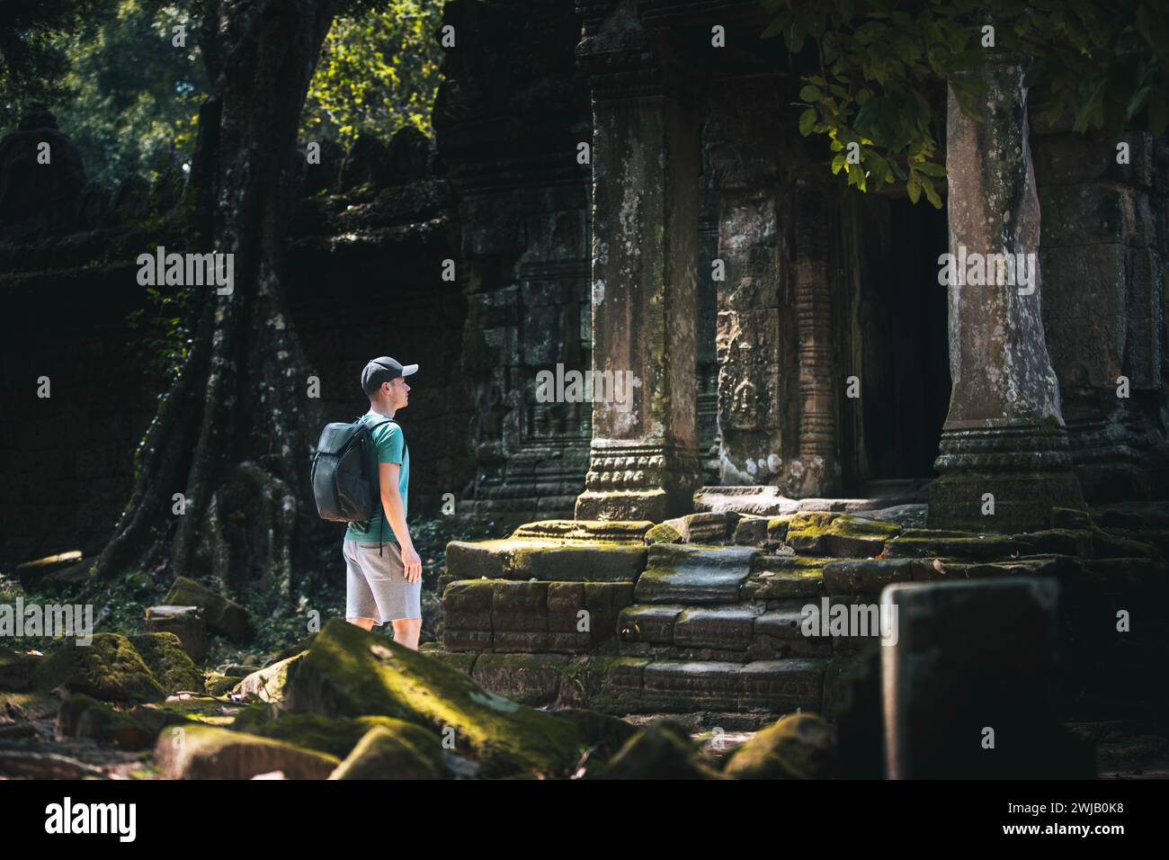 Reisende in Kambodscha. Mann mit Rucksack, der antike Tempelruinen bewundert, die von tropischem Grün bewachsen sind. Stockfoto