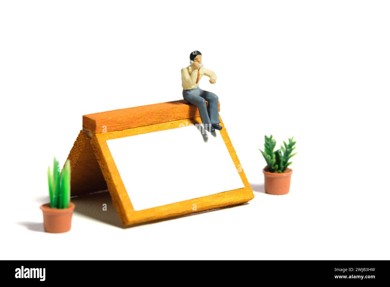 Miniatur-Kleinkinder-Spielfiguren-Fotografie. Konzept zur Erinnerung an den Zeitplan für Telefonanrufe. Ein Geschäftsmann telefoniert über dem Kalender des Schreibtischs. Stockfoto