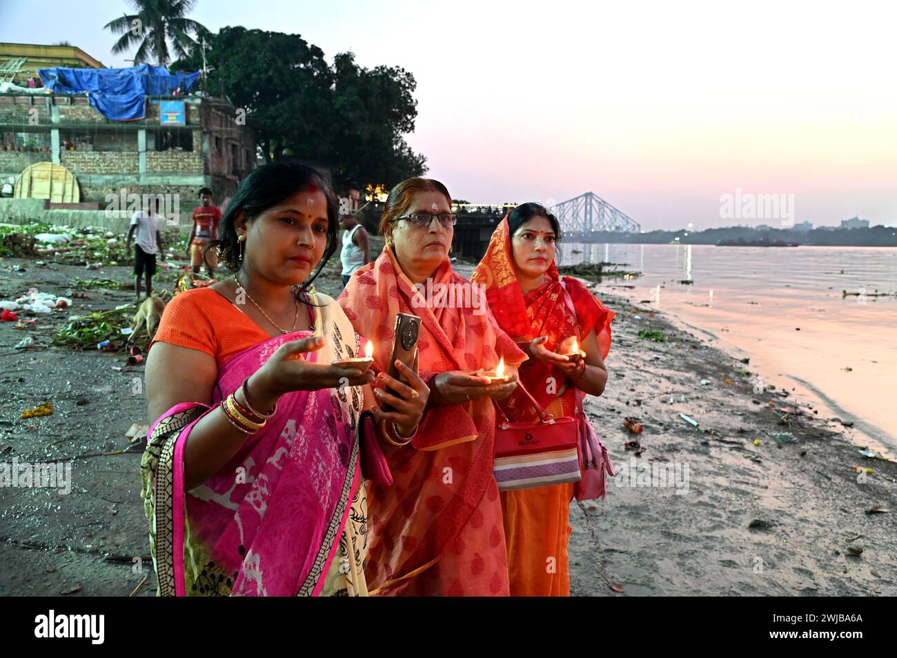 Indische Frauen, die Abendgebete mit einer schwimmenden Lehmlampe am Ufer des Ganges in Kalkutta, Indien, durchführen. Stockfoto