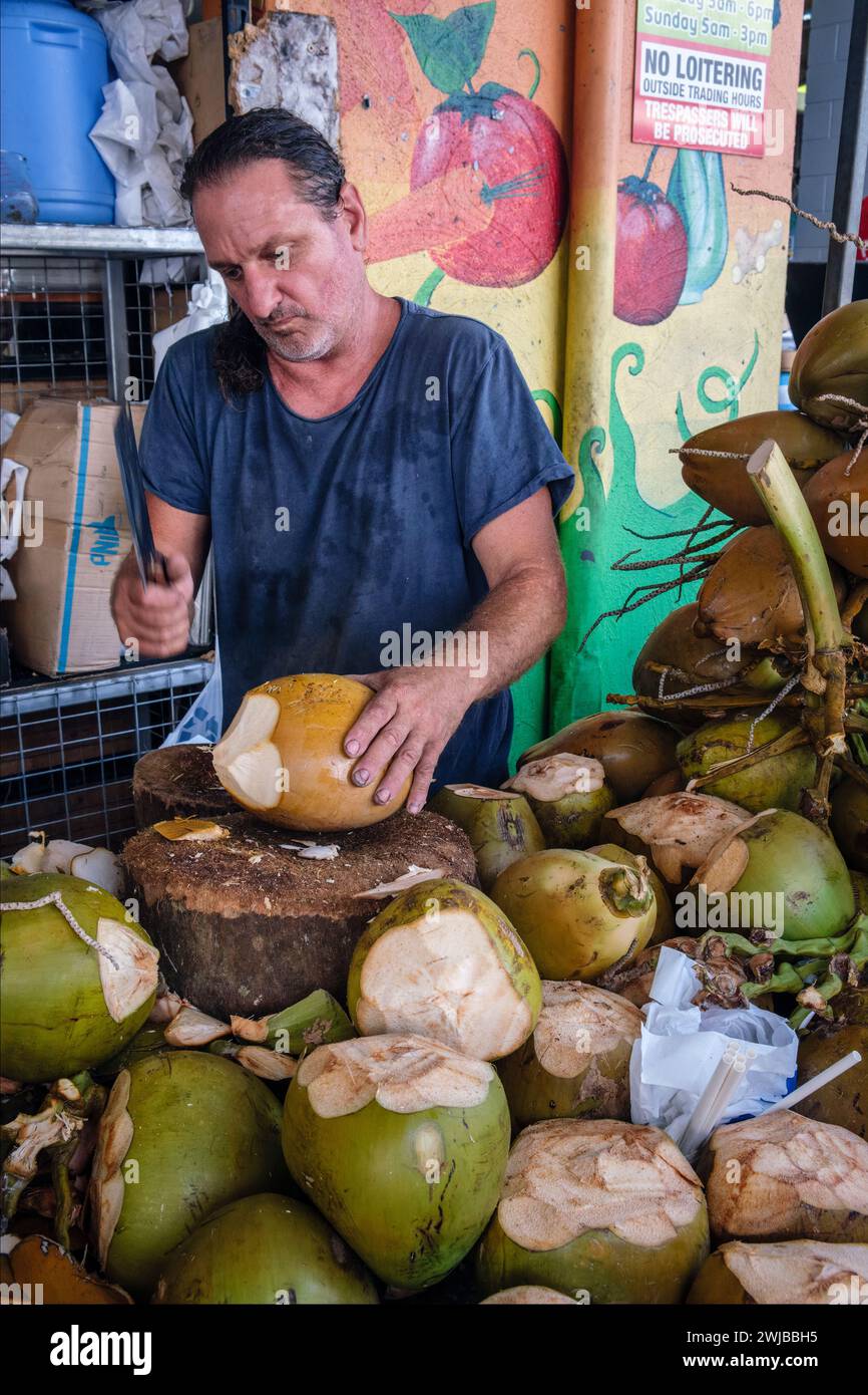 Ein Stände, der Kokosnüsse auf seinem Stall in Rusty's Markets, Cairns, Queensland, Australien öffnet Stockfoto