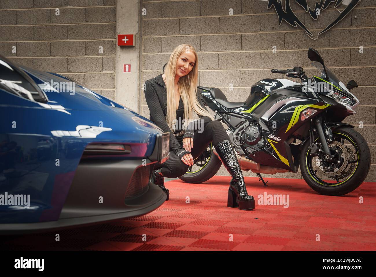 Blonde Dame mit Kawasaki Bike und Porsche 911 GT3 in ihrer Garage Stockfoto