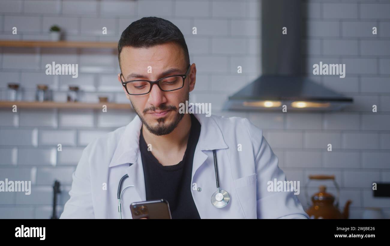 Männliche Ärzte tragen weiße Uniform mit Stethoskop, das im Internet auf dem Handy surft, E-Mails liest, Mediennachrichten liest, soziale Netzwerke scrollt, verwendet Stockfoto