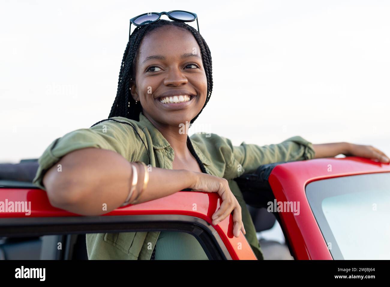 Die junge Afroamerikanerin lehnt sich auf einem roten Auto auf einer Autofahrt Stockfoto