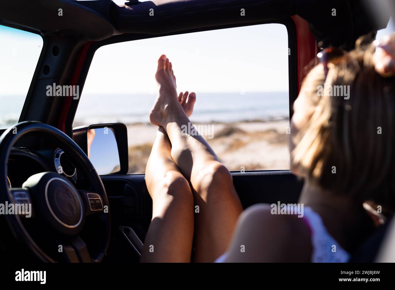 Junge kaukasische Frau entspannt sich in einem Auto am Strand auf einem Roadtrip Stockfoto
