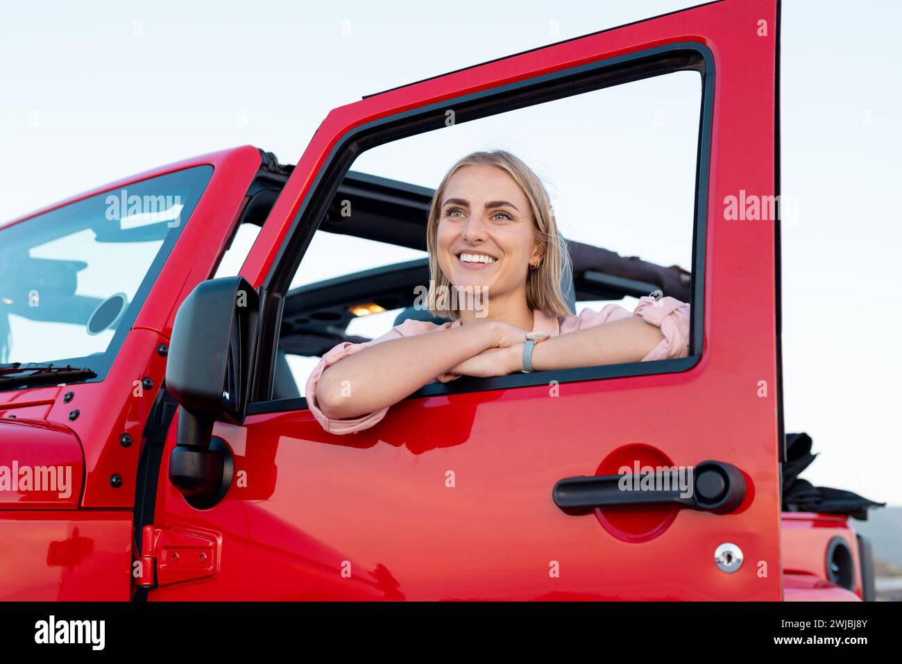 Die junge kaukasische Frau lächelt auf einer Fahrt aus einem roten Fahrzeugfenster Stockfoto