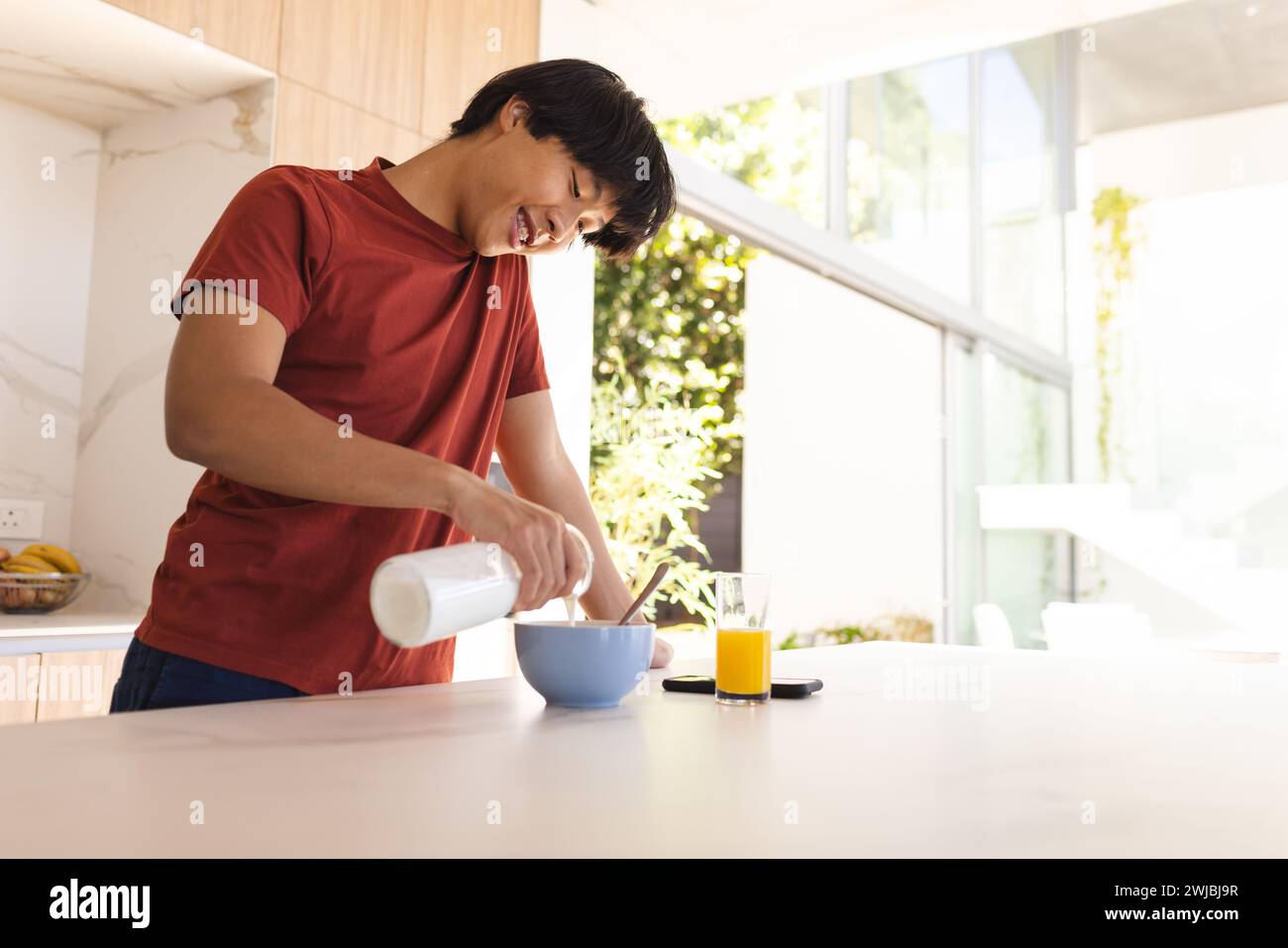 Teenager Asiatischer Junge gießt Milch in eine Schüssel zu Hause, mit Kopierraum Stockfoto