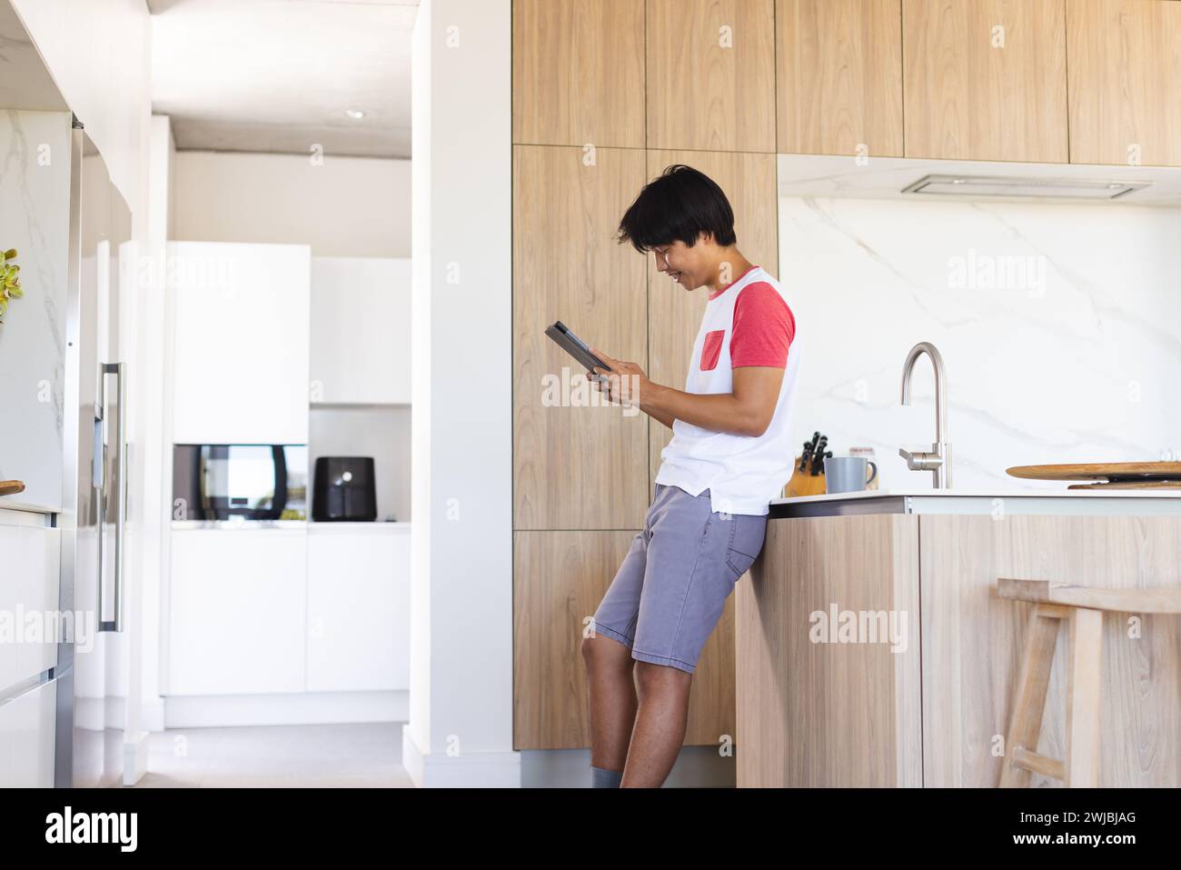Ein Teenager asiatischer Junge sucht sein Tablet in einer modernen Küche Stockfoto