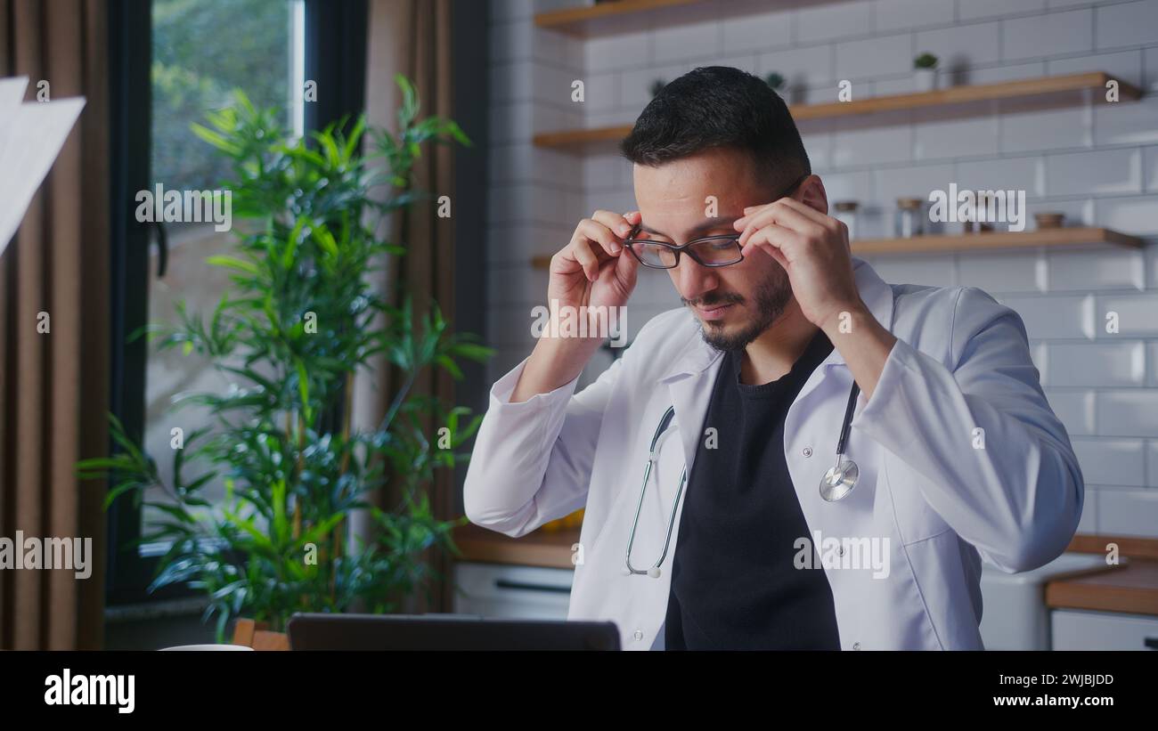Erfahrener Arzt mit Brille in weißem Mantel, der von seiner Assistentin Patientenberichte abnimmt und untersucht. Männlicher Praktizierender, der Papierkram macht Stockfoto