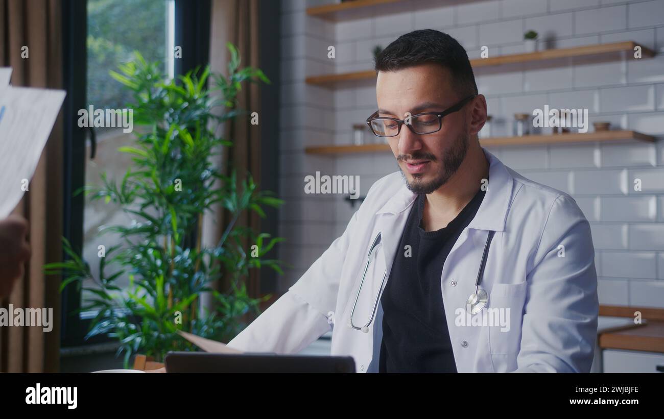 Erfahrener männlicher Arzt mit Brille in weißem Mantel, der Patientenberichte von seiner Assistentin und Untersuchungen annimmt. Männlicher Praktizierender, der Papierkram macht Stockfoto