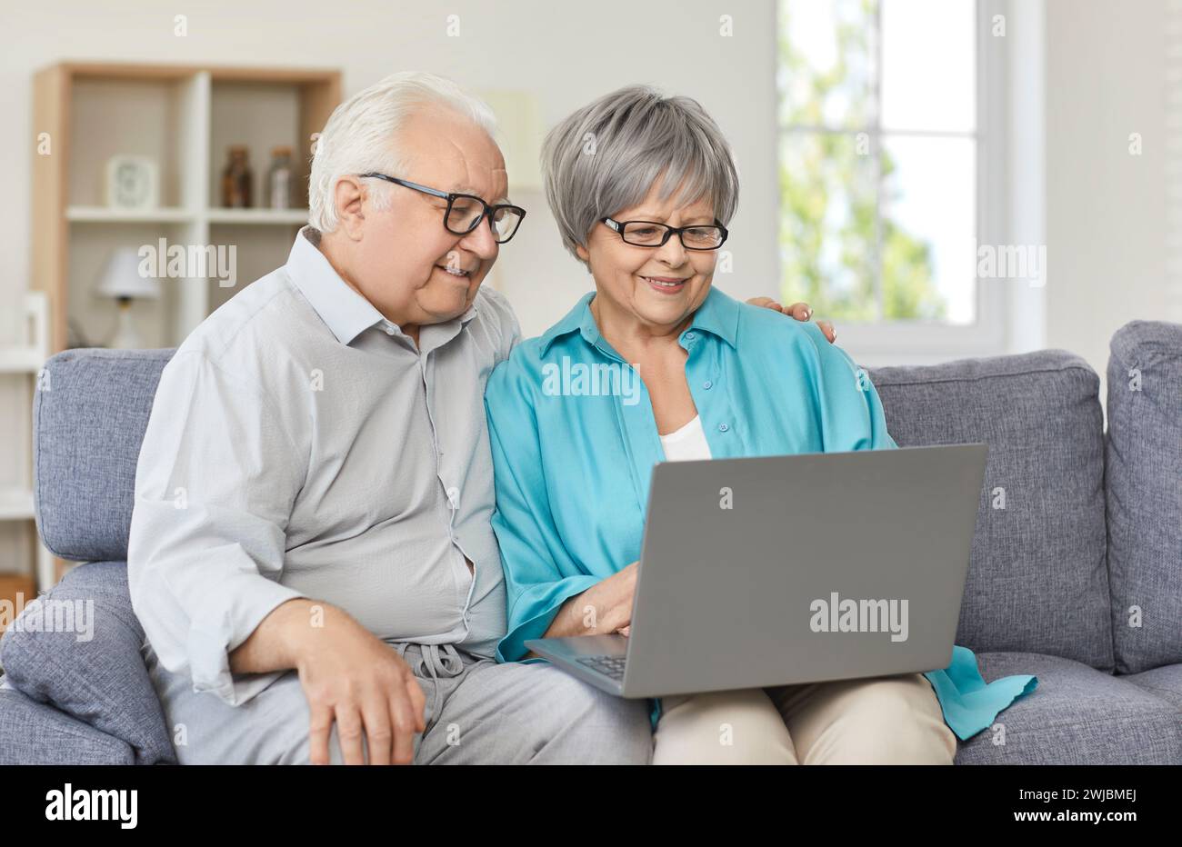 Glückliches Seniorenpaar, das auf der Couch sitzt und zusammen ihren Laptop ansieht Stockfoto