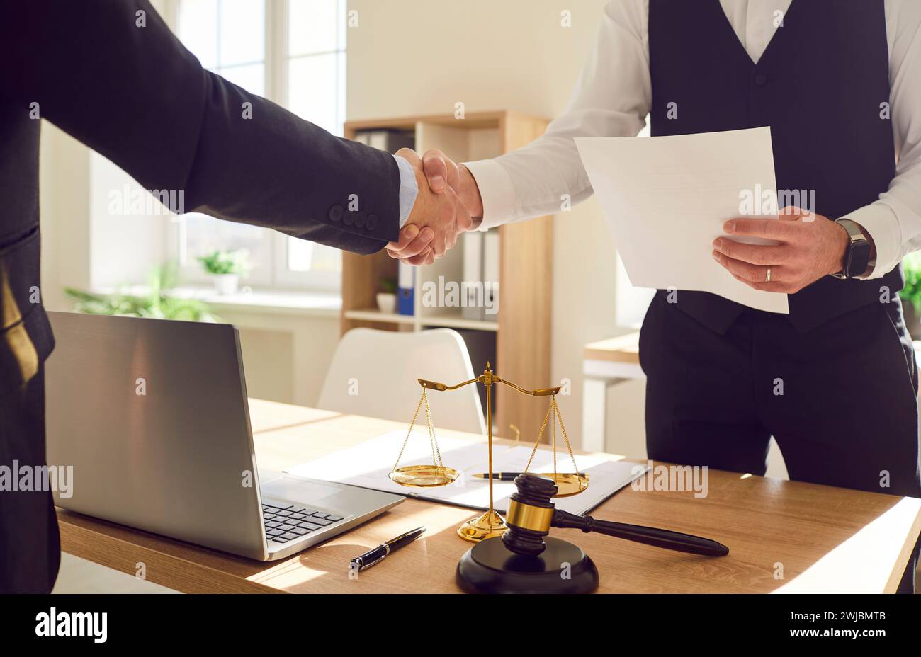 Männlicher Anwalt, der im Büro arbeitet, schüttelt Hand mit einem männlichen Klienten, der am Schreibtisch am Arbeitsplatz steht Stockfoto