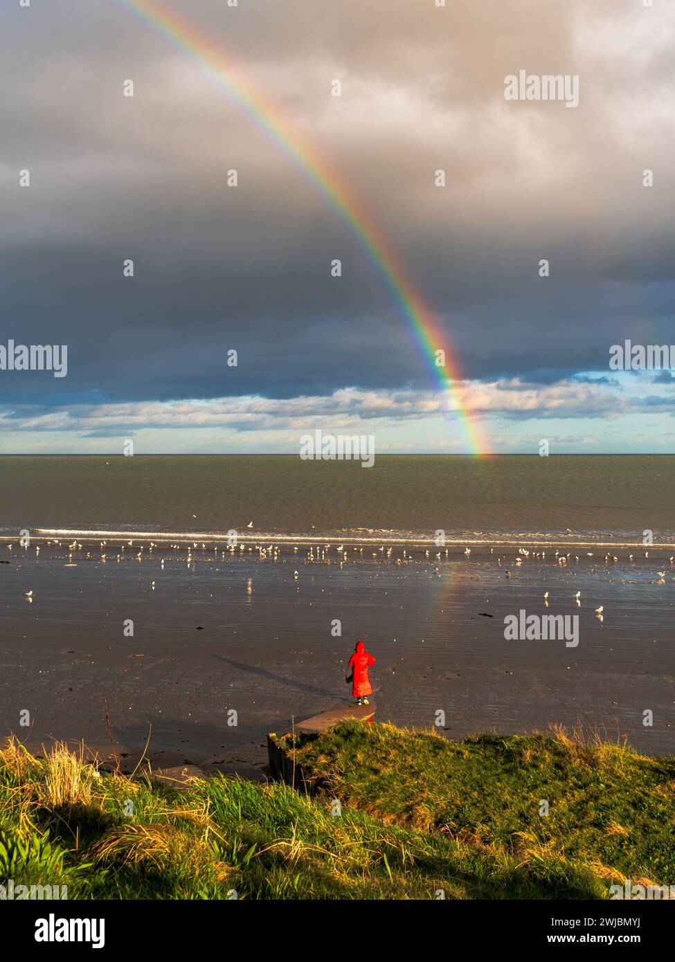 Die Dame in Rot mit einem Regenbogen über der Irischen See am Portmarnock Beach Stockfoto