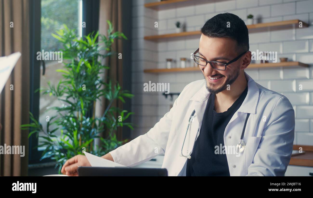 Lächelnder Arzt mit Brille in weißem Mantel, der Patientenberichte von seiner Assistentin nimmt und untersucht. Männlicher Praktizierender, der Papierkram macht Stockfoto