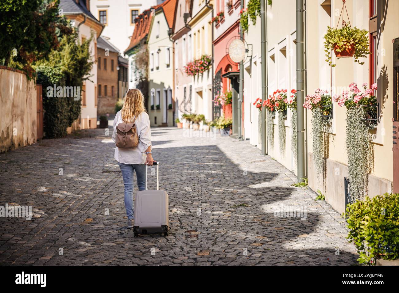 Alleinreisen. Frau, die auf der Straße unterwegs ist, mit Koffer und Rucksack. Reisen und Urlaub in der europäischen Stadt Olomouc, Tschechische Republik Stockfoto