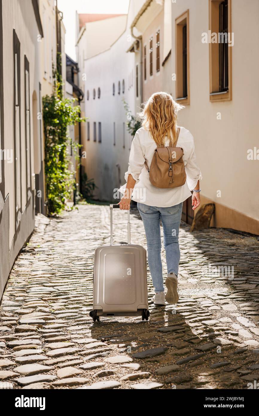 Alleinreisen. Frau, die auf der Straße unterwegs ist, mit Koffer und Rucksack. Reisen und Urlaub in der europäischen Stadt Olomouc, Tschechische Republik Stockfoto