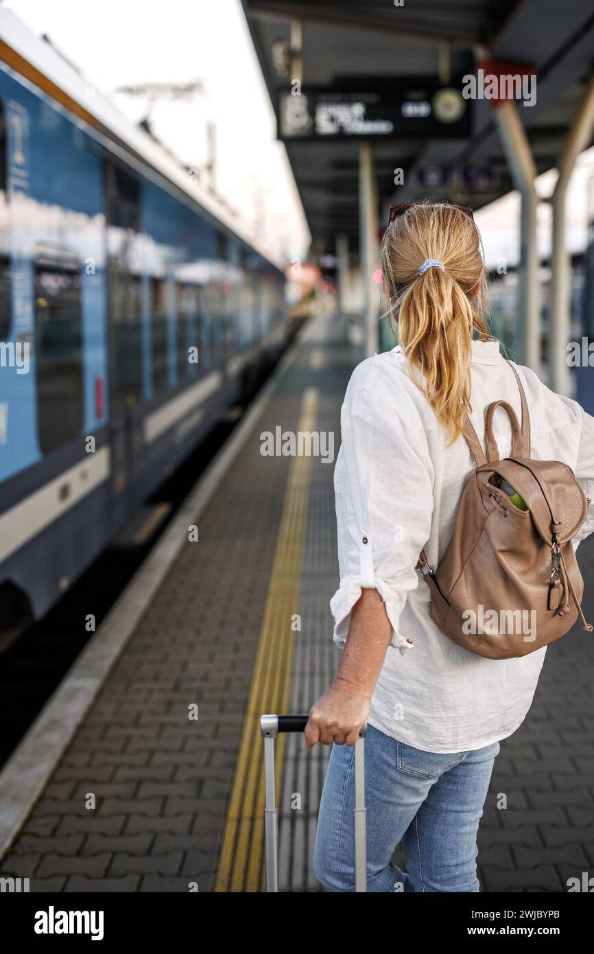 Frau, die mit dem Zug reist. Touristen mit Rucksack und Koffer, die am Bahnsteig des Bahnhofs zum Einsteigen in den Zug warten. Alleinreisender Lifestyle Stockfoto