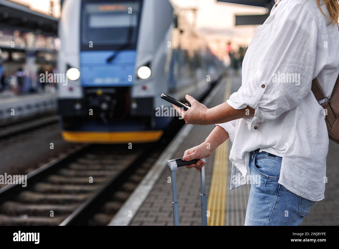 Frau mit Koffer kauft online ein Ticket für den Transport per Smartphone und mobile App. Touristen warten am Bahnhof auf den Zug. Alleinreisen Stockfoto