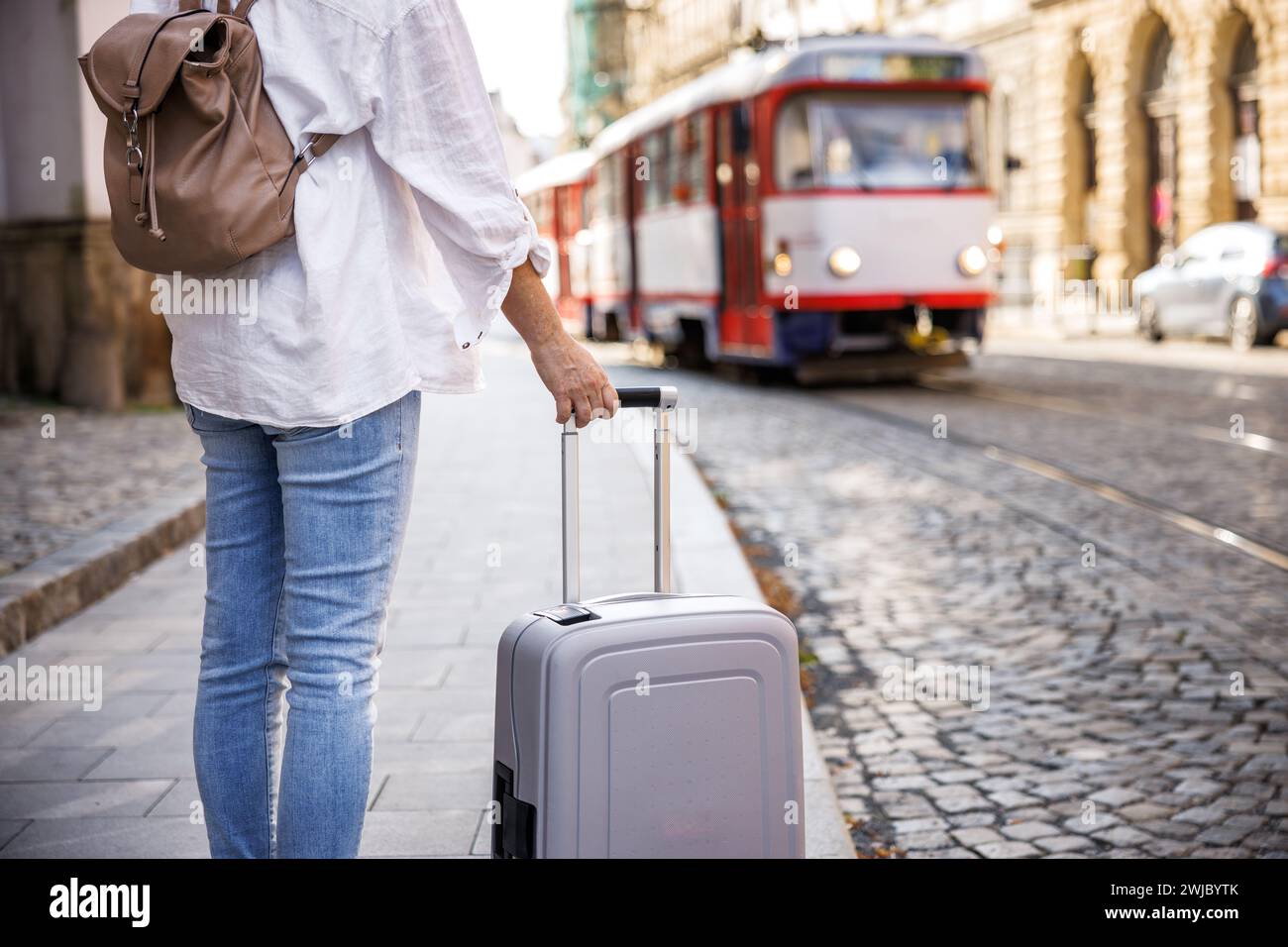 Frau, die auf der Straße auf die Straßenbahn wartet, mit Koffer und Rucksack. Fahrt mit öffentlichen Verkehrsmitteln in der Stadt Stockfoto