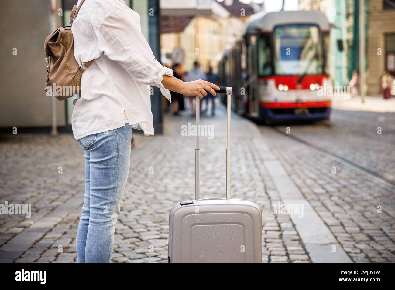 Fahrt mit öffentlichen Verkehrsmitteln in der Stadt. Frau, die auf der Straße auf die Straßenbahn wartet, mit Koffer und Rucksack Stockfoto