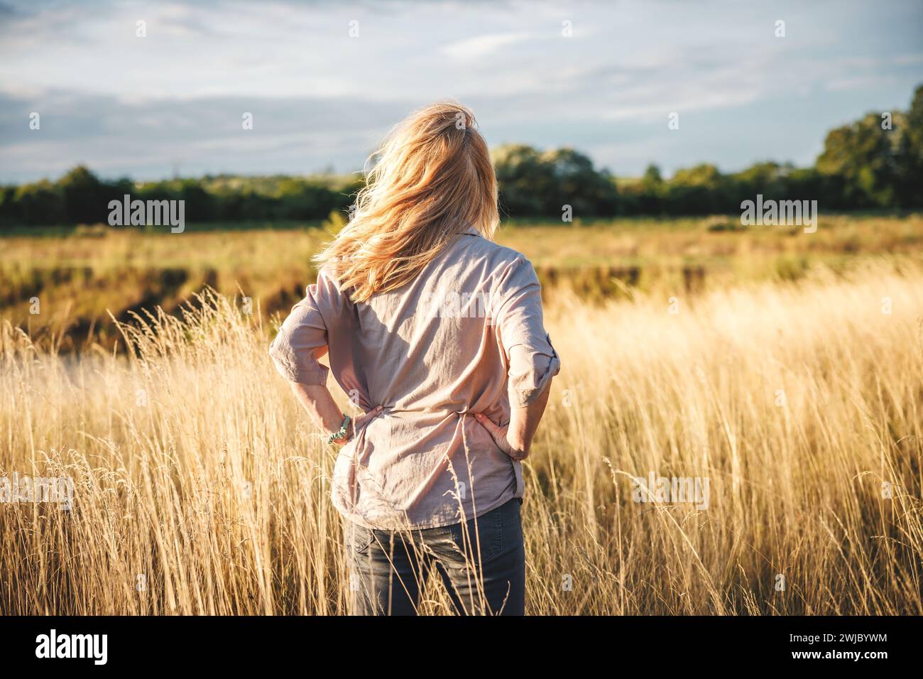 Frau, die im Gras steht im Wind und fühlt Verbundenheit und Harmonie mit der Natur Stockfoto