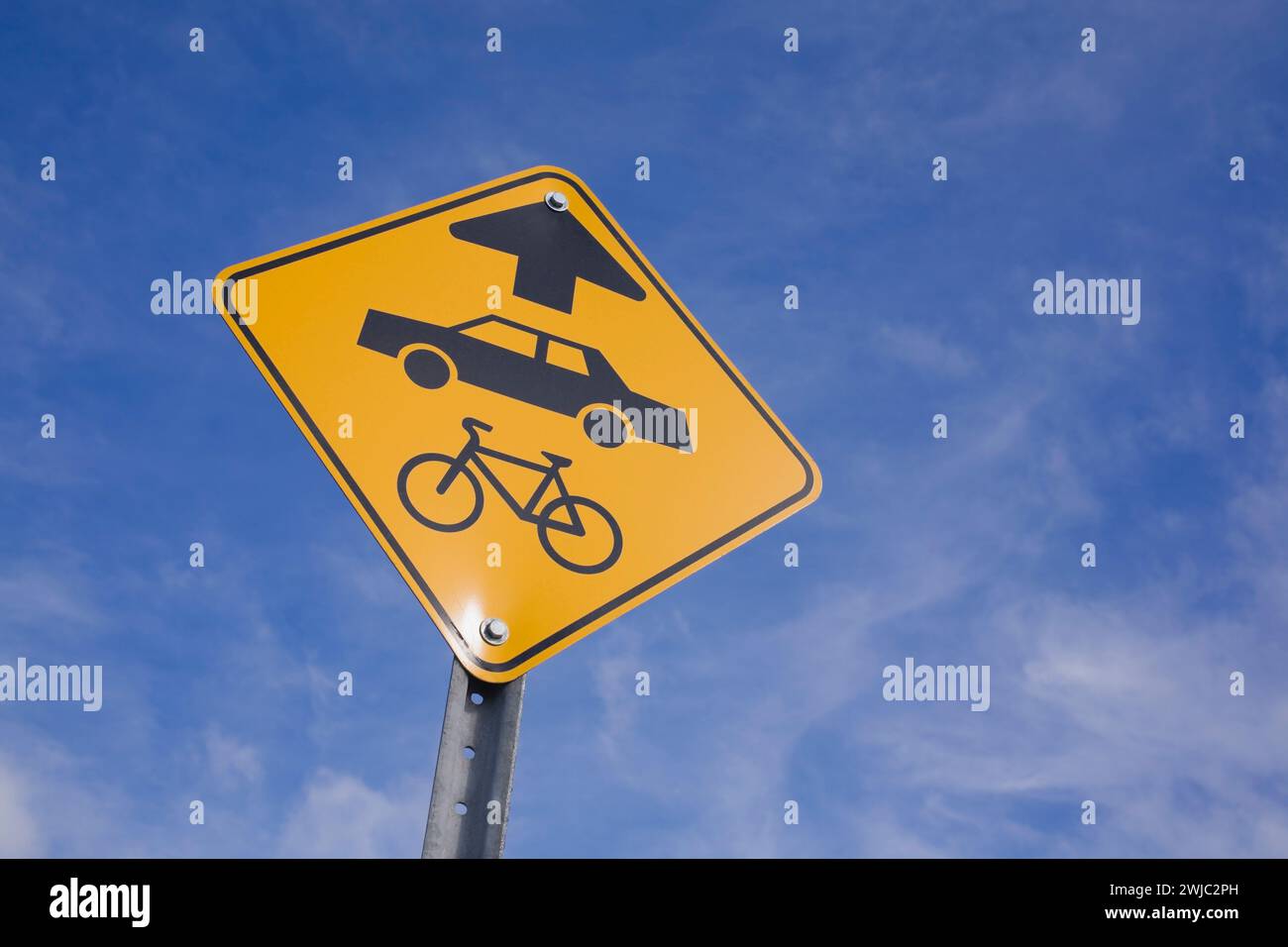 Gelbes Verkehrspiktogramm mit schwarz lackiertem Auto, Fahrrad und Richtungspfeil, das eine gemeinsame Umlaufbahn anzeigt. Stockfoto