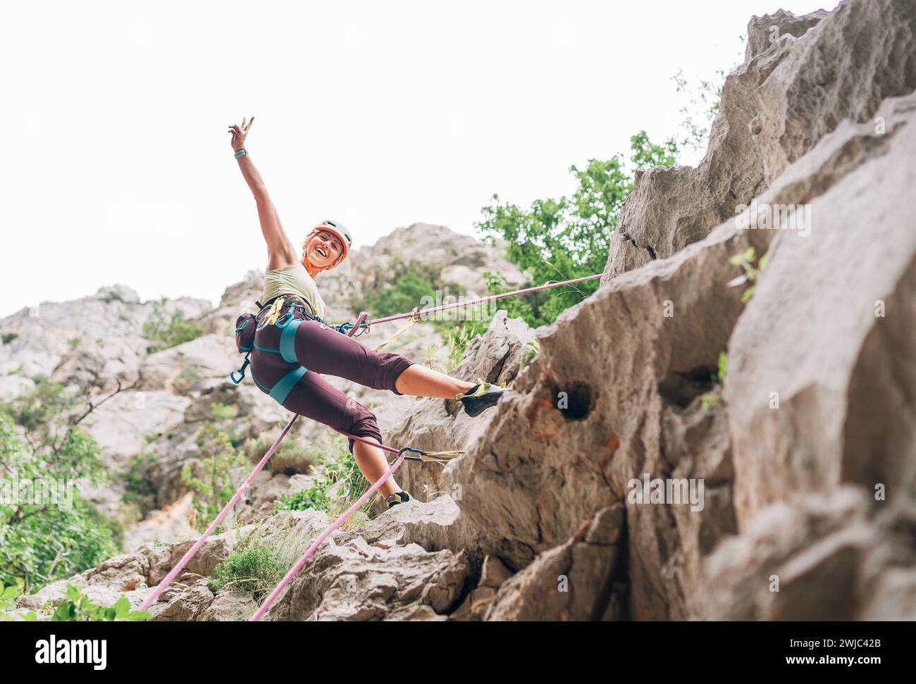 Lächelnde Sportlerin in Schutzhelm und -Schuhen Klettern auf die Felswand mit Seil und Gurtzeug im Paklenica-Nationalpark in Kroatien. Stockfoto