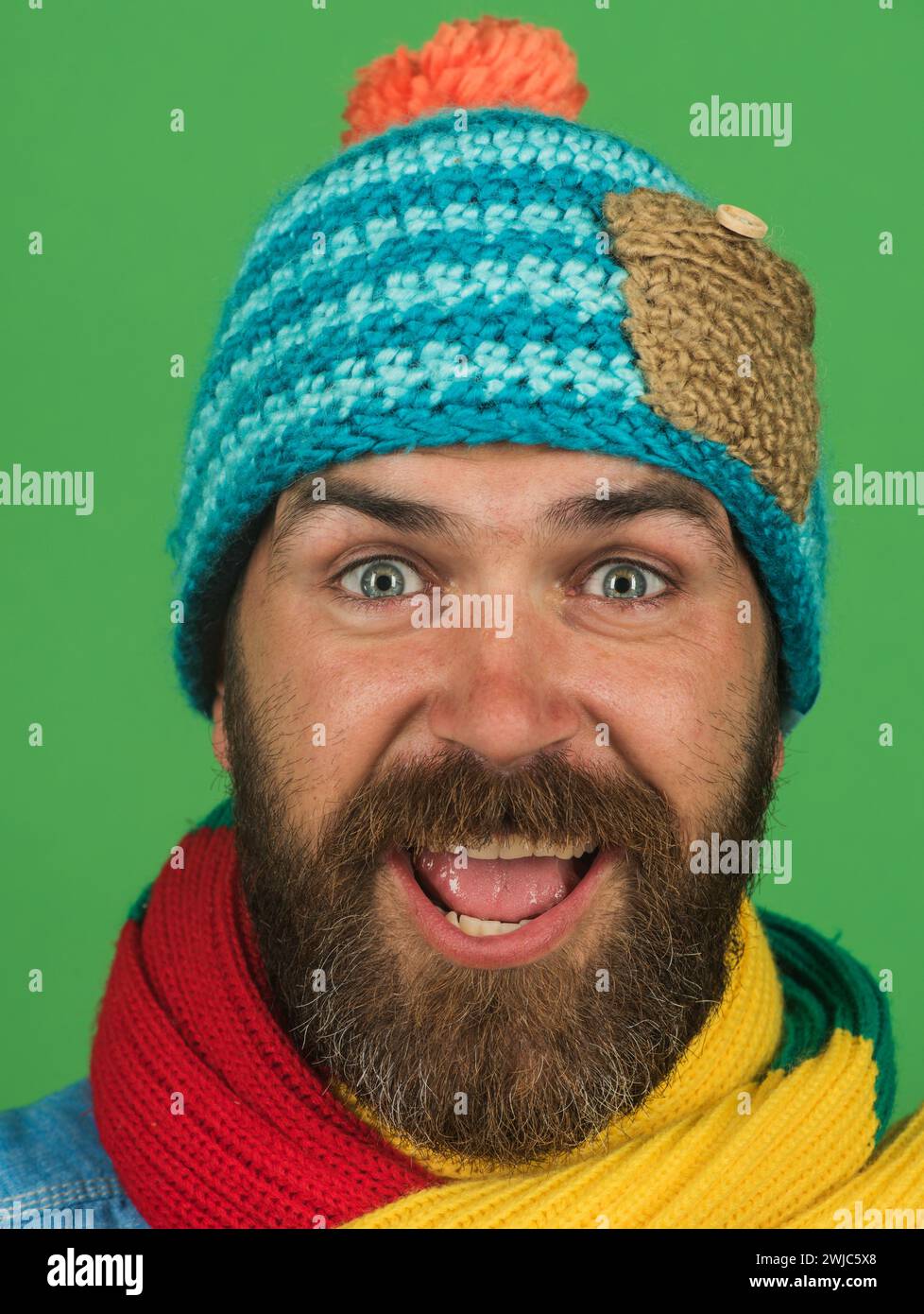 Porträt eines gutaussehenden Mannes mit Bart in Strickmütze und Schal. Glücklicher bärtiger Mann in farbenfrohem Schal und Wollmütze. Modischer Mann in Winterkleidung Stockfoto