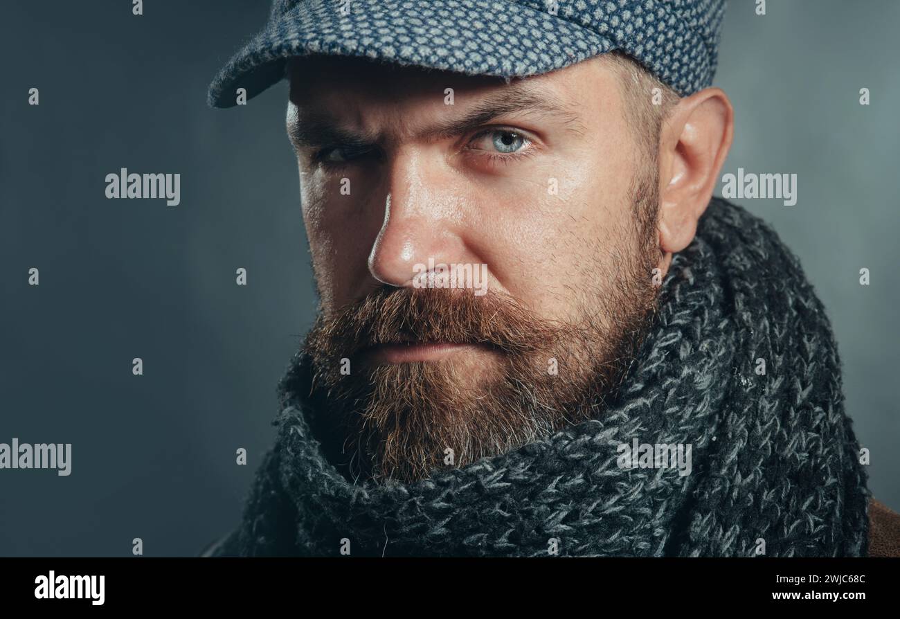 Nahaufnahme Porträt eines ernsten Mannes mit Bart in Mütze und Schal. Winteraccessoires. Hübscher bärtiger Mann mit grauem Schal und Hut. Attraktiver männlicher in Stockfoto