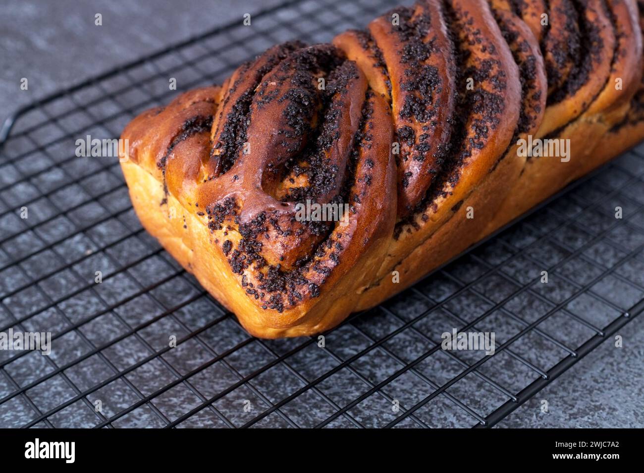 Ein ganzes Brötchen mit Mohnfüllung liegt auf einem heißen Stand, schwarzer Hintergrund, Draufsicht Stockfoto