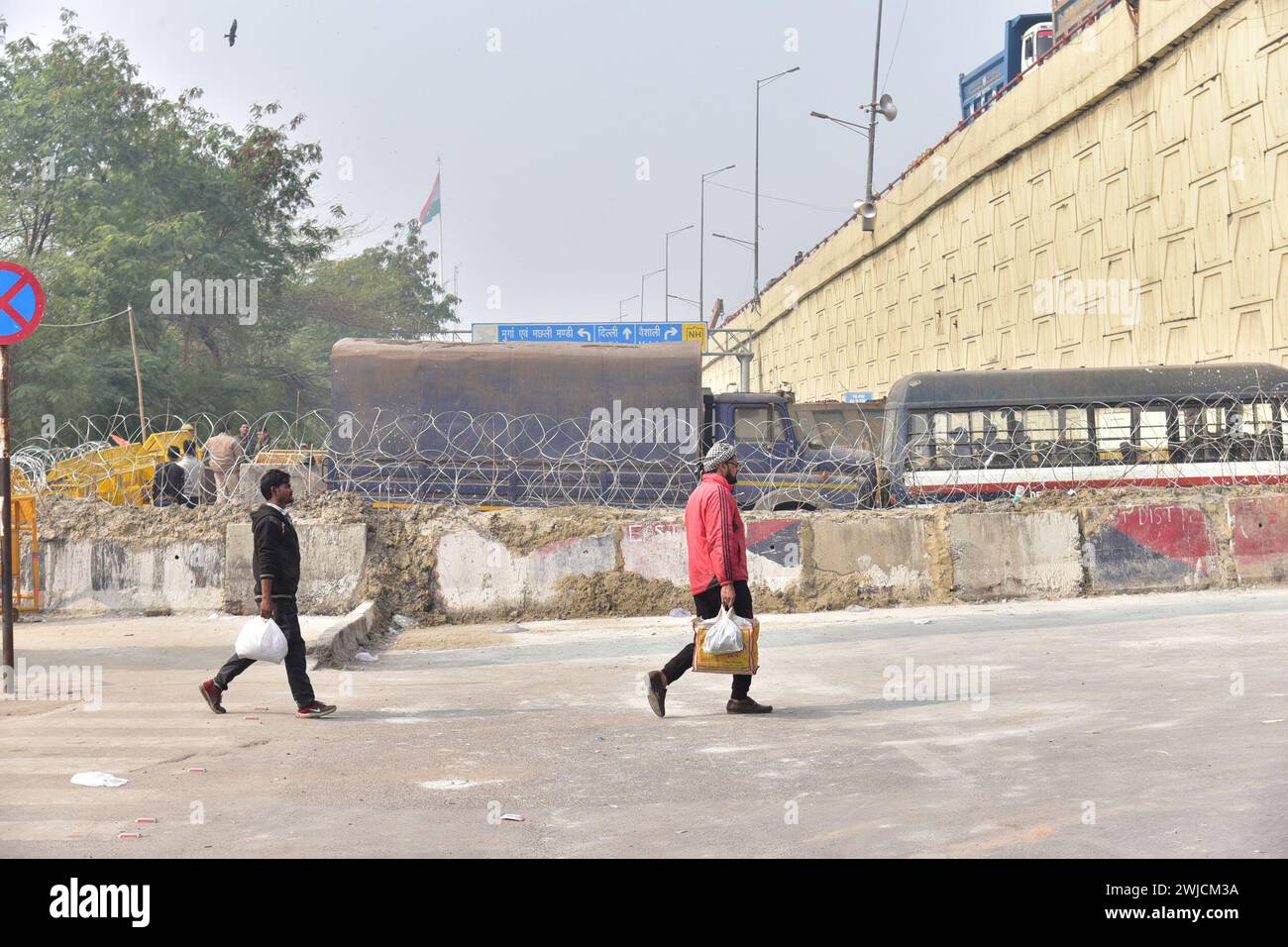 GHAZIABAD, INDIEN – 14. FEBRUAR 2024: Menschen gehen zu Fuß wegen Barrikaden an der Grenze zu Delhi Ghazipur in Ghaziabad, Indien. Massive Einsätze von Polizei und paramilitärischem Personal, neben mehrschichtigen Barrikaden, haben stattgefunden, um die Landeshauptstädte Singhu, Tikri und Ghazipur zu besiegeln, um die protestierenden Bauern am Eindringen in die Stadt während ihres geplanten "Delhi Chalo"-marsches am Dienstag zu hindern. Die Polizei von Delhi hat bis zum 12. März auch Abschnitt 144 der Strafprozessordnung in der ganzen Stadt verhängt und jede Art von Kundgebung oder Prozession sowie die Blockade verboten Stockfoto