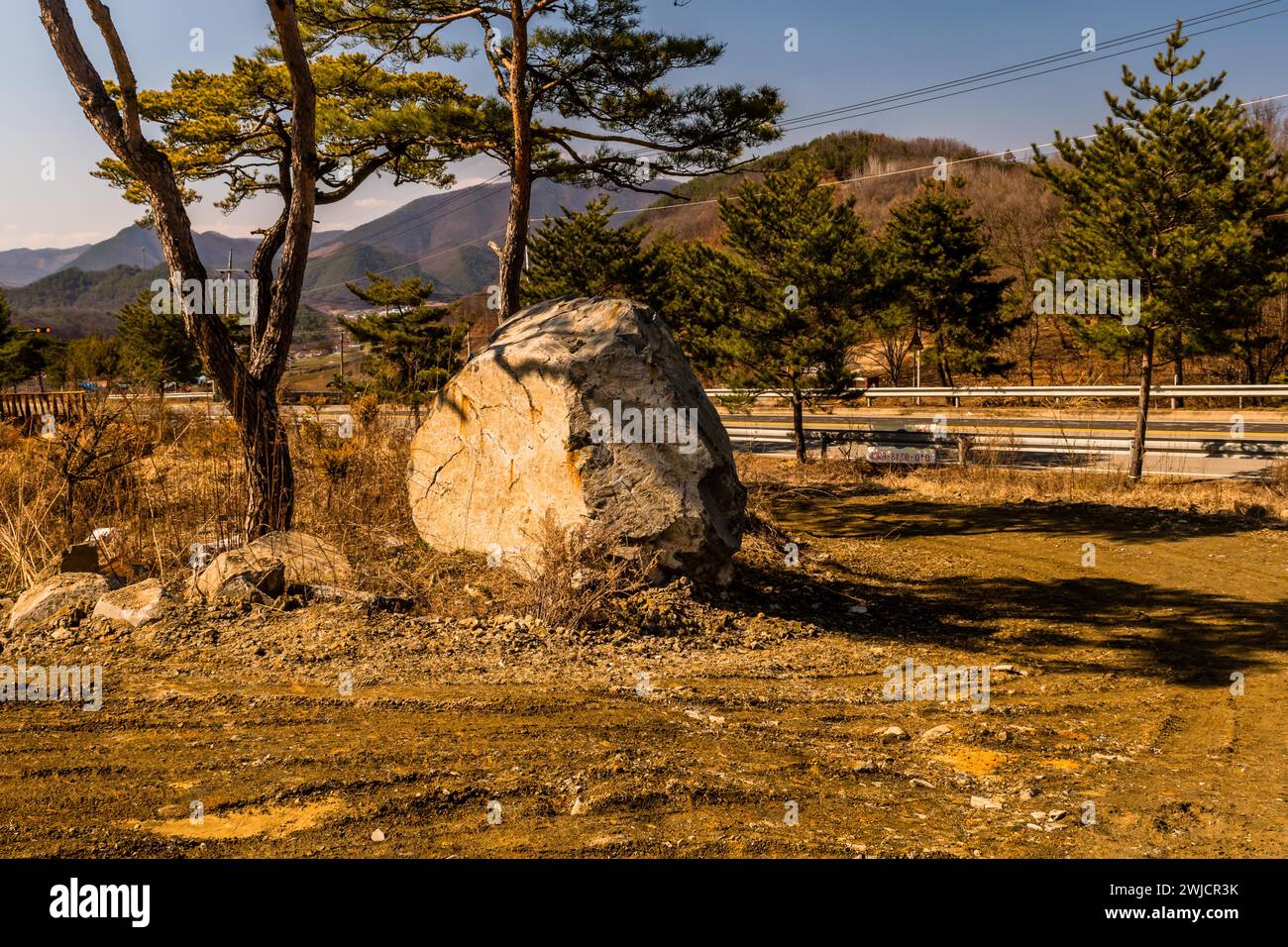 Großer Granitfelsen im Schatten der Bäume neben der Landstraße an sonnigen Tagen in Südkorea Stockfoto