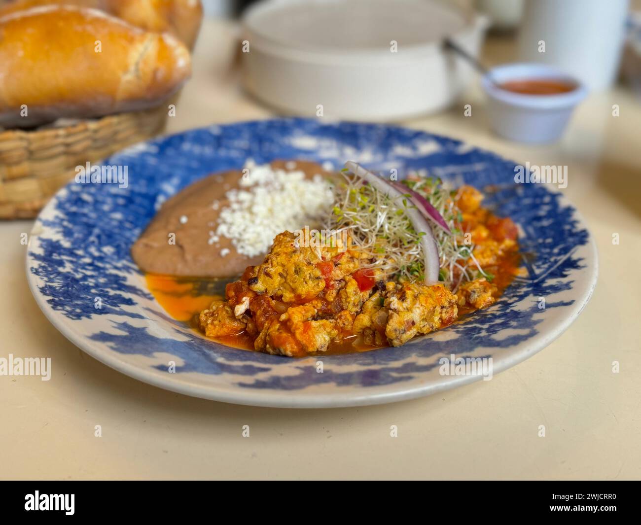 Nahaufnahme eines herzhaften mexikanischen Frühstücksplattes mit Rührei mit Carne Seca, Tomaten, Zwiebeln und einer Seite mit frisch gebackenen Bohnen, garniert mit Käse Stockfoto