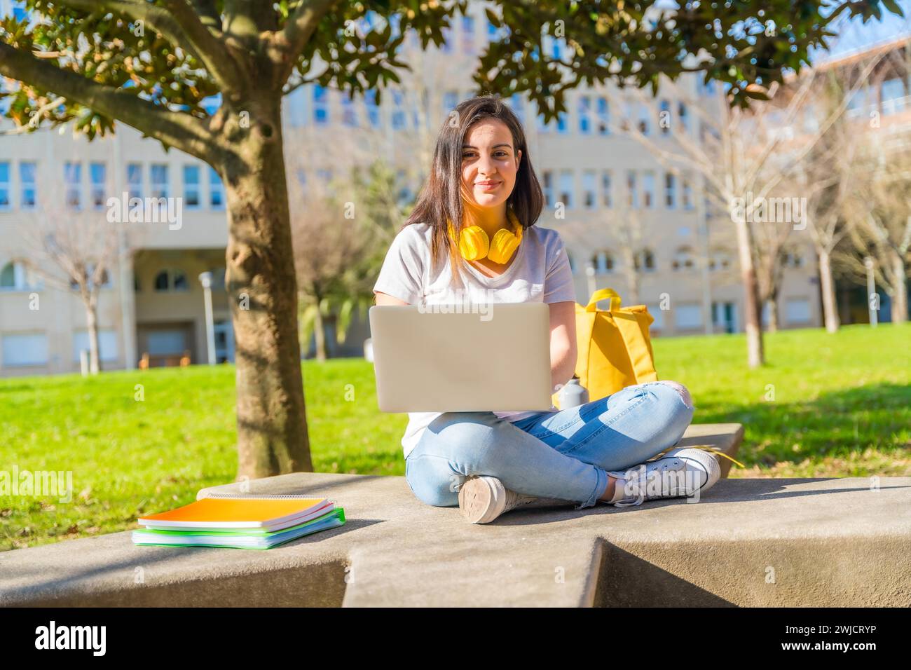 Porträt eines fröhlichen Studenten mit Laptop, der auf dem Boden vor dem Campus sitzt Stockfoto