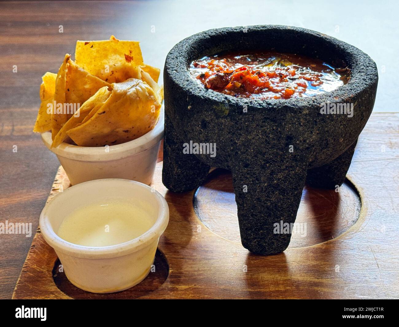 Traditionelle mexikanische Molcajete-Schüssel gefüllt mit frischer Salsa, begleitet von knusprigen Maistortilla-Chips und einer Seite cremiger Sauce, servierfertig. Stockfoto