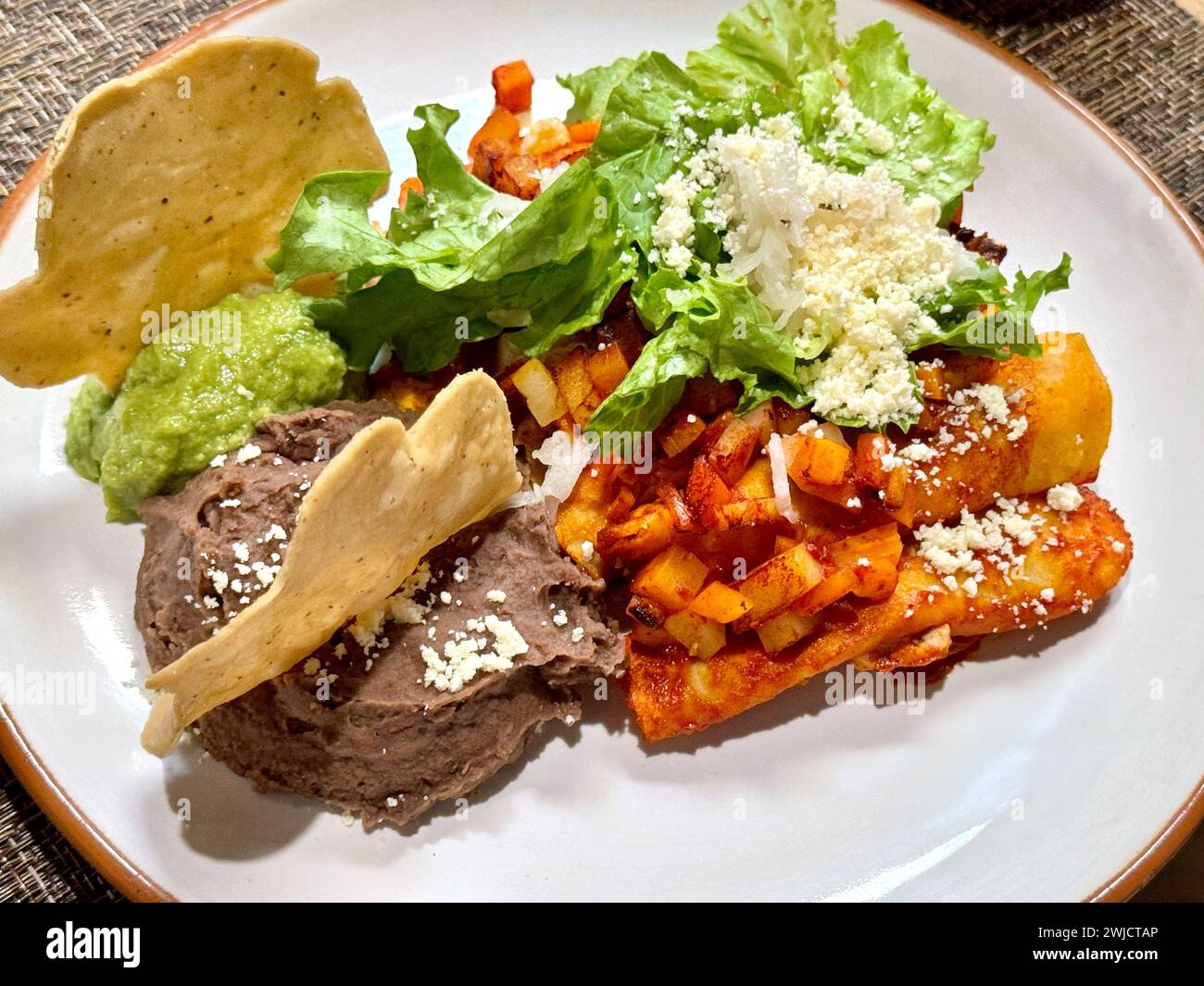 Herzhafte Enchiladas mit roter Sauce, gepaart mit cremigen, frischen Guacamole, knusprigen Totopos und zerbröckeltem Queso Fresco. Stockfoto