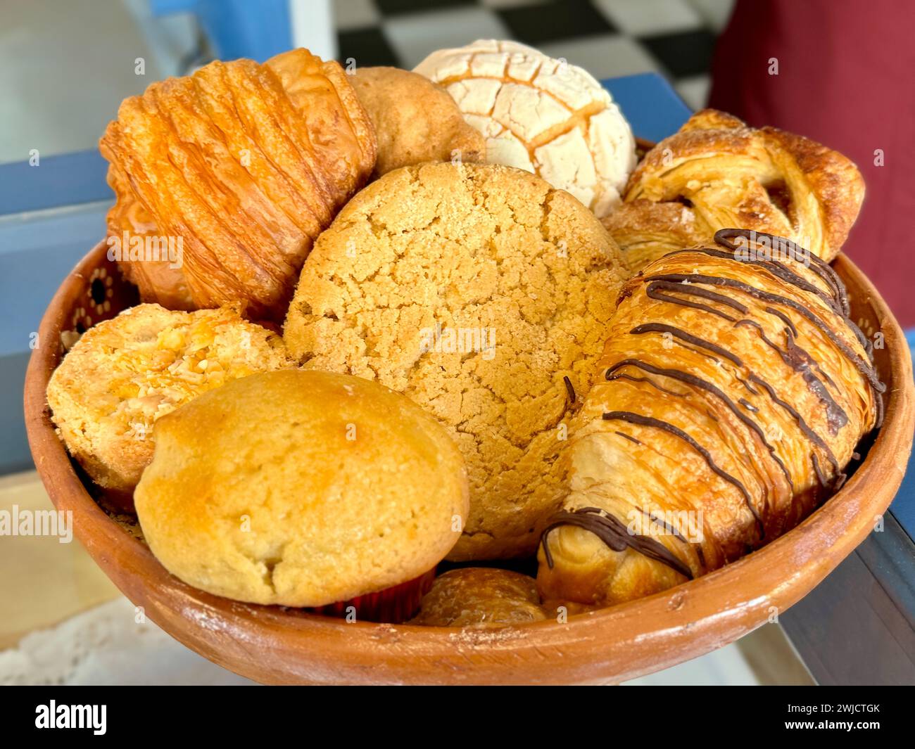 Nahaufnahme einer verlockenden Auswahl mexikanischer Süßbrote, darunter conchas, Gebäck und Muffins, serviert in einem traditionellen Tongericht. Stockfoto