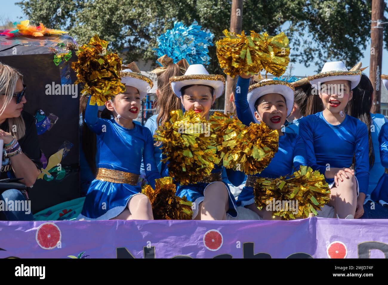 Junge Mädchen, die Cowboyhüte tragen und goldene Pompons winken, fahren 2024 auf einem Wagen in der Parade of Orangen, Teil der 92. Texas Citrus Fiesta, Mission, Texas USA. Stockfoto