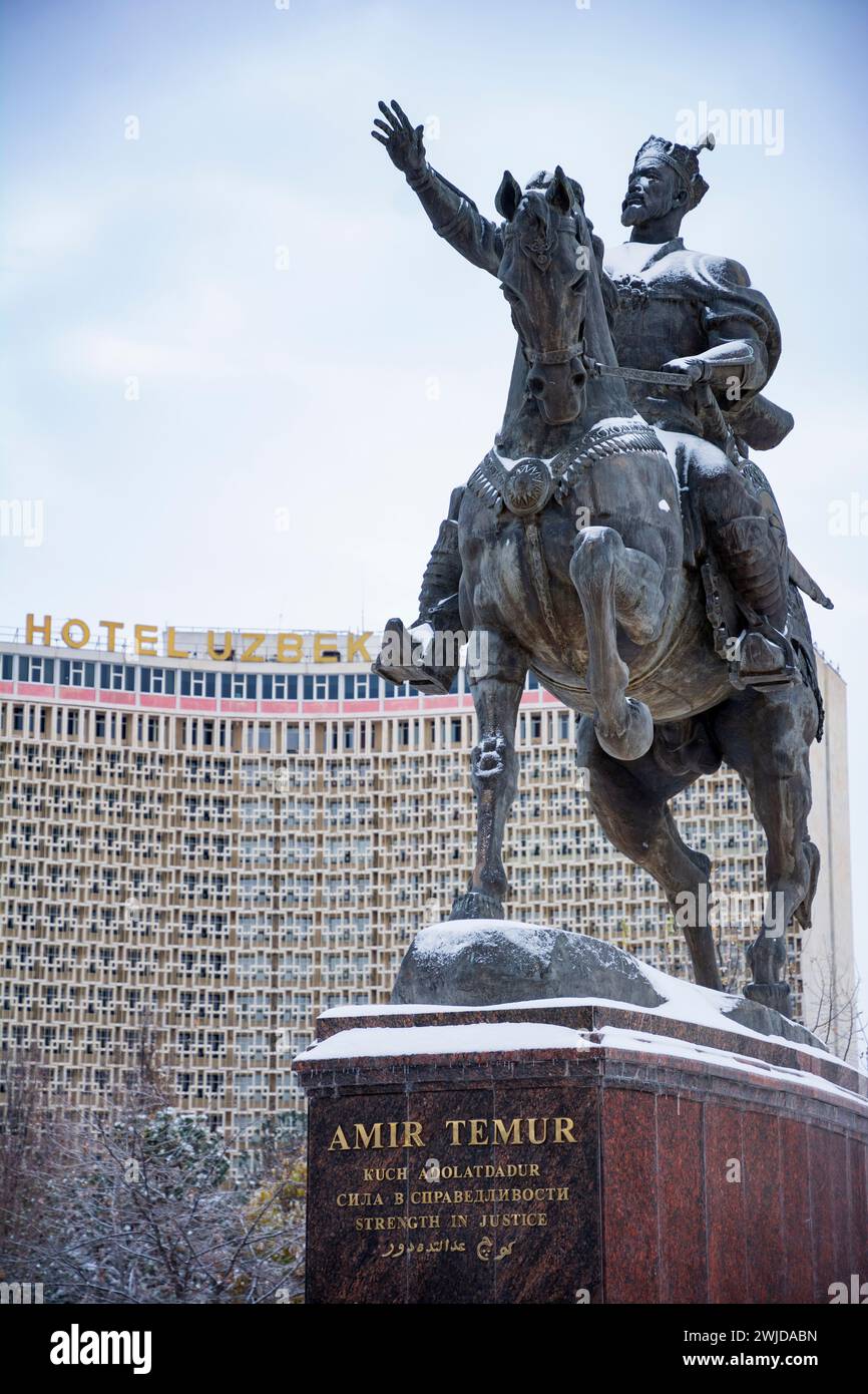 Die Statue von Amir Timur (Tamerlane) bedeckt mit Schnee, mit dem berühmten Hotel Usbekistan als Kulisse Stockfoto