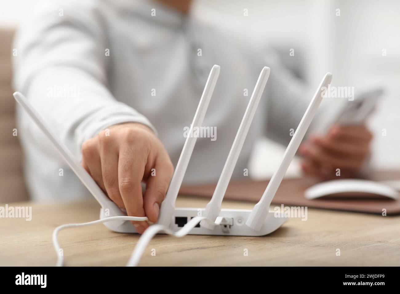 Mann, der Kabel in den WLAN-Router an einem Holztisch drinnen steckt, Nahaufnahme Stockfoto