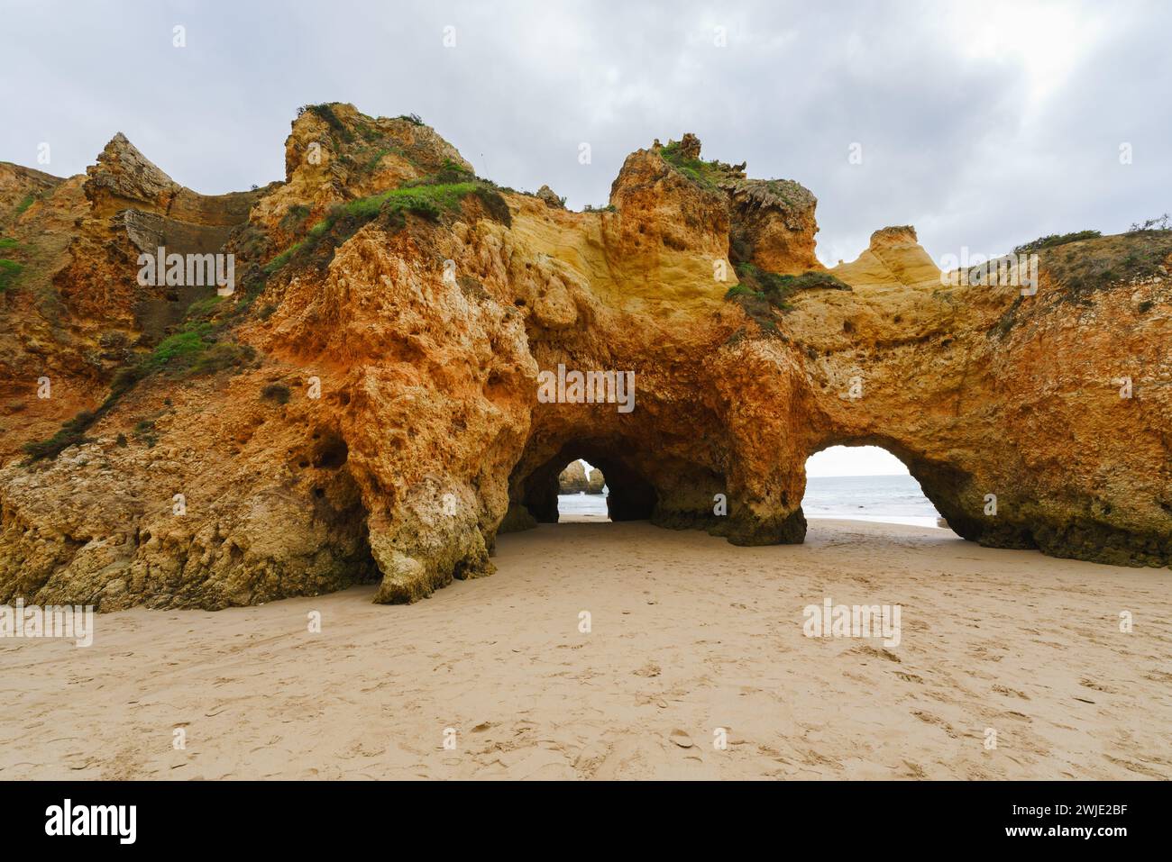 Raue Küstenszene mit hoch aufragenden Bögen, versteckten Höhlen, stürzenden Wellen und einem dramatischen bewölkten Himmel, Algarve, Portugal Stockfoto
