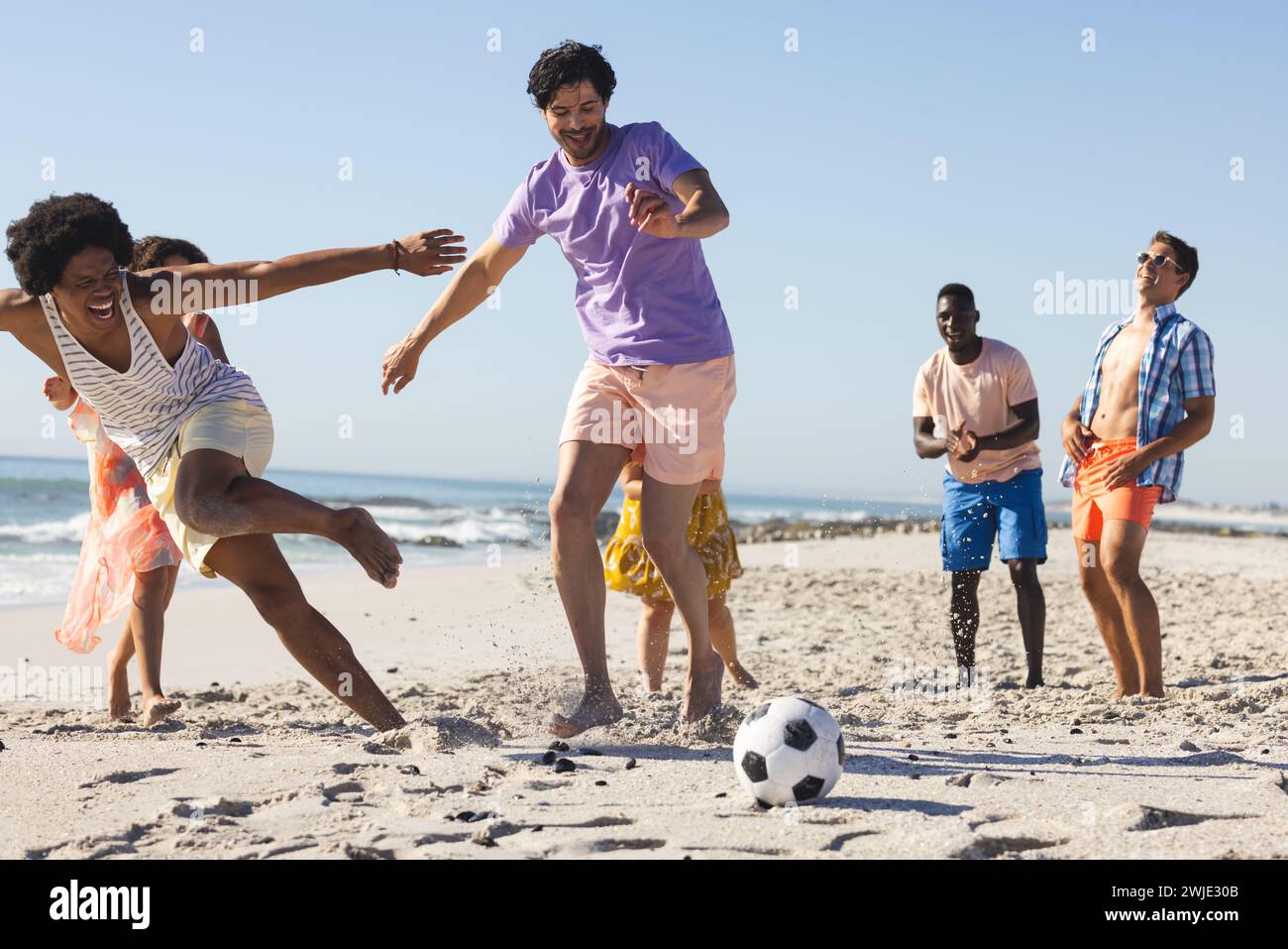 Vielfältige Freunde genießen ein spielerisches Fußballspiel am Strand Stockfoto