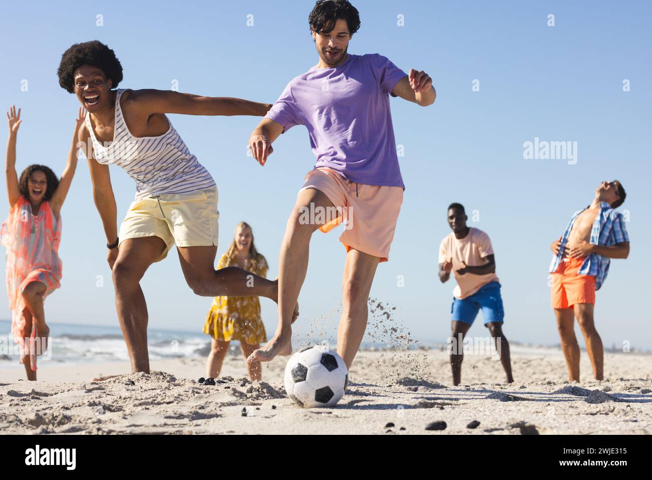 Vielfältige Freunde genießen ein lebhaftes Fußballspiel am Strand Stockfoto