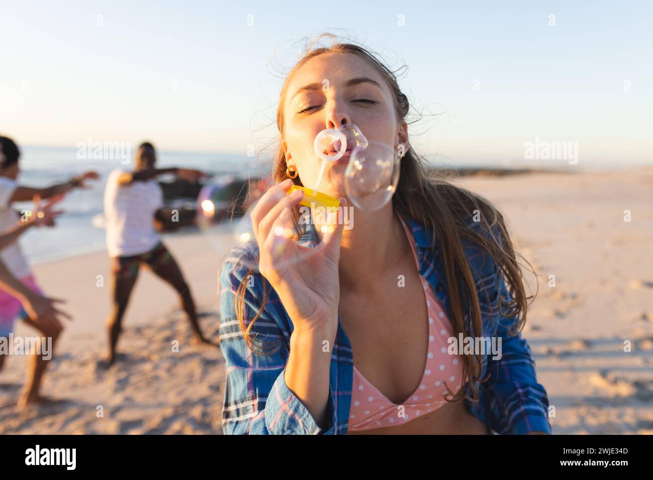 Junge kaukasische Frau bläst Blasen an einem sonnigen Strand Stockfoto
