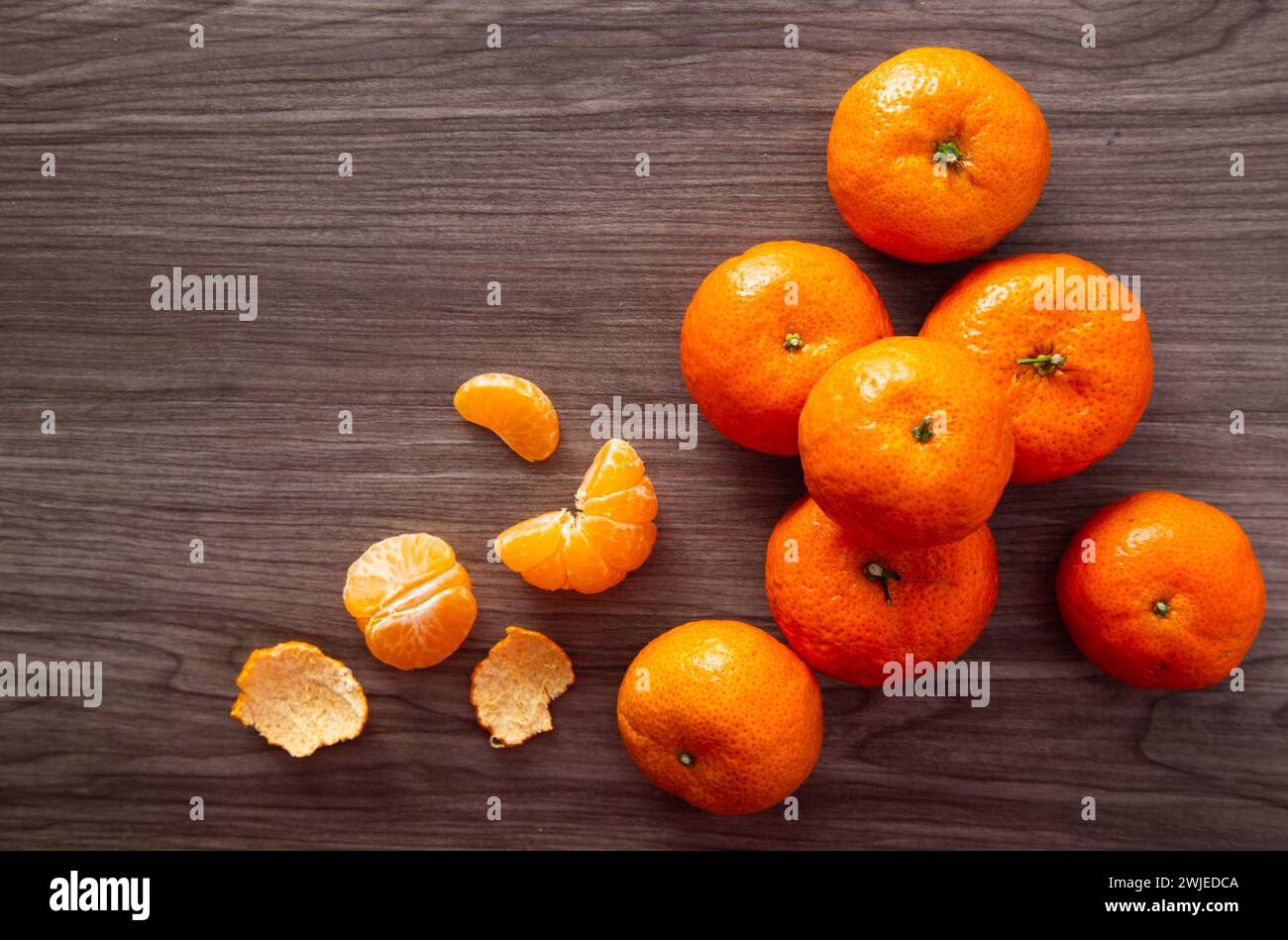 Tangerinen und geschälte Stücke liegen auf einer dunklen Holzoberfläche Stockfoto