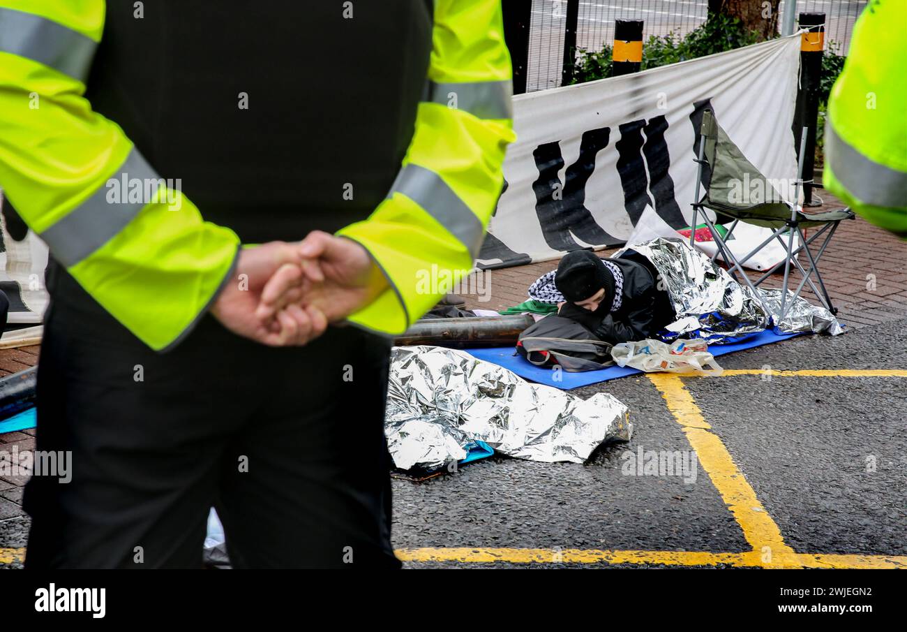 Polizisten bilden eine Absperrung, während sie auf die Ankunft des Schneideteams warten, während ein Demonstrant in eine Wärmebüche und eine Metallverriegelung gewickelt wird. Unterstützer der Palästinensischen Aktion blockieren den einzigen Fahrzeugzugang zur israelischen Verteidigungsfirma, dem Geschäft von Elbit Systems in Aztec West, Bristol. Sie argumentieren, dass die von Elbit in Großbritannien hergestellten Waffen von der israelischen Verteidigungsstreitkräfte gegen Palästinenser in Gaza und anderswo eingesetzt werden. Bei den israelischen Bombenanschlägen im Gazastreifen sind seit Oktober 2023 mehr als 30.000 Palästinenser ums Leben gekommen. Die Palästinensische Aktion ist entschlossen, Elbit und ihren Partner c unnachgiebig ins Visier zu nehmen Stockfoto