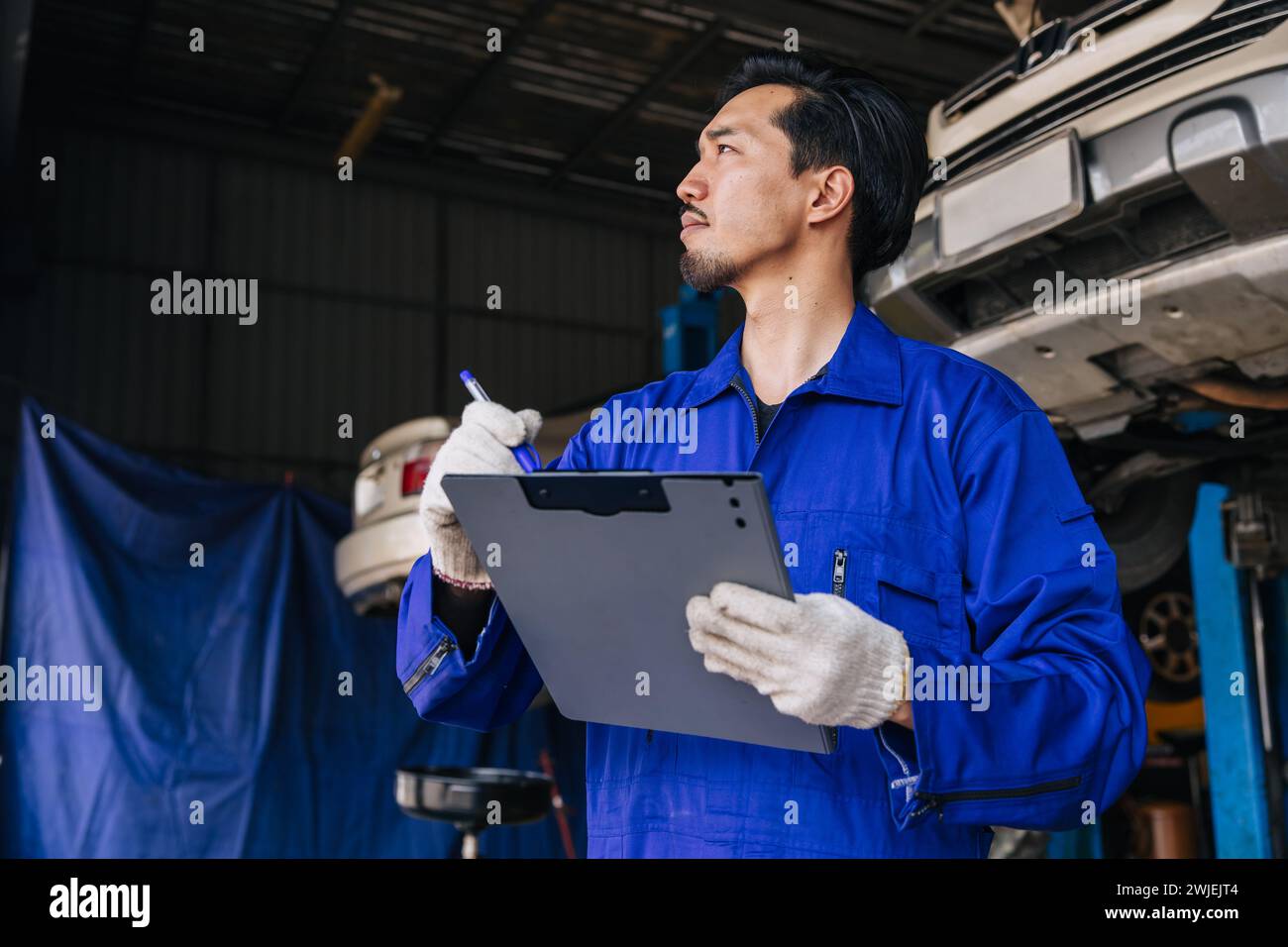 Asiatischer japanischer Mechaniker männlicher Arbeiter Angestellter, der Auto in Auto Service Werkstatt Wartung überprüft, ersetzen Sie Reparatur Auto-Teil-Checkliste Stockfoto